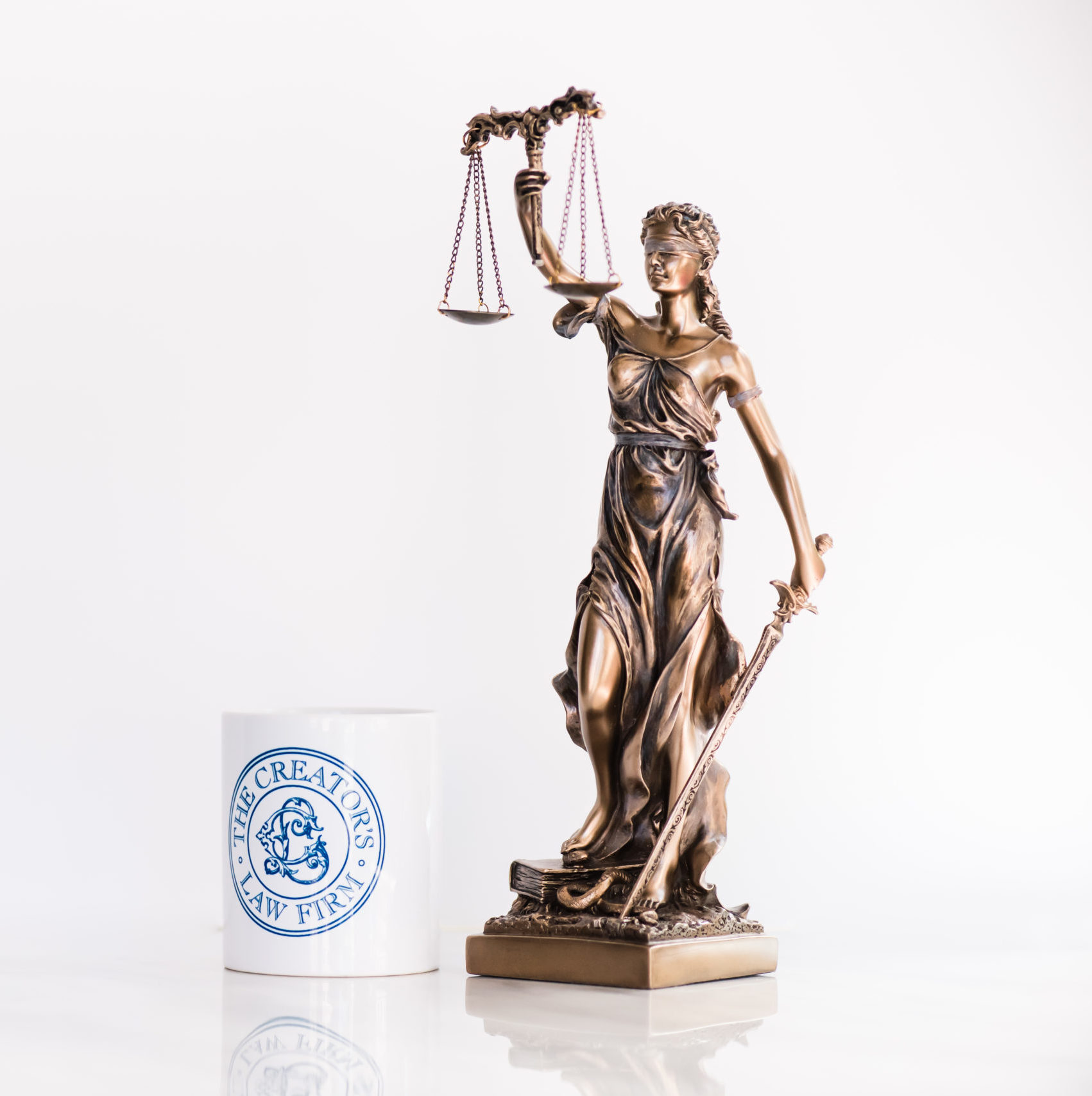 Mini statute of lady justice next to a coffee cup with the creators law firm logo